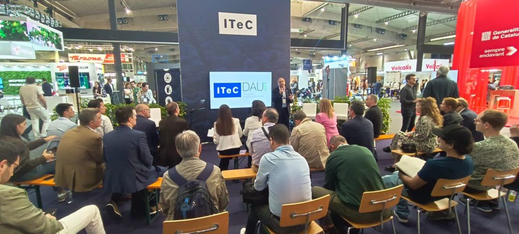 Asistentes sentados frente al stand del ITeC en Construmat 2024 durante una ponencia sobre documentación técnica en el sector de la construcción.