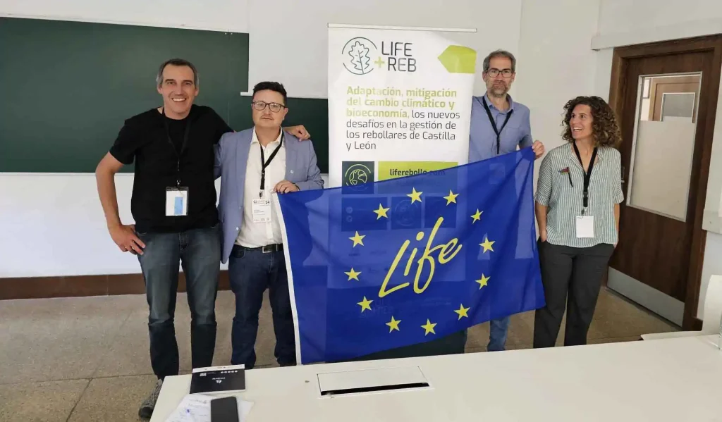 Cuatro participantes en el CIMAD 2024 posan con una bandera de la Unión Europea y un rollup de un proyecto LIFE detrás, en un encuentro de networking sobre proyectos LIFE forestales.
