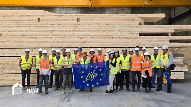 Participantes con cascos y chalecos sostienen la bandera LIFE UE delante de paneles de madera en Legutio