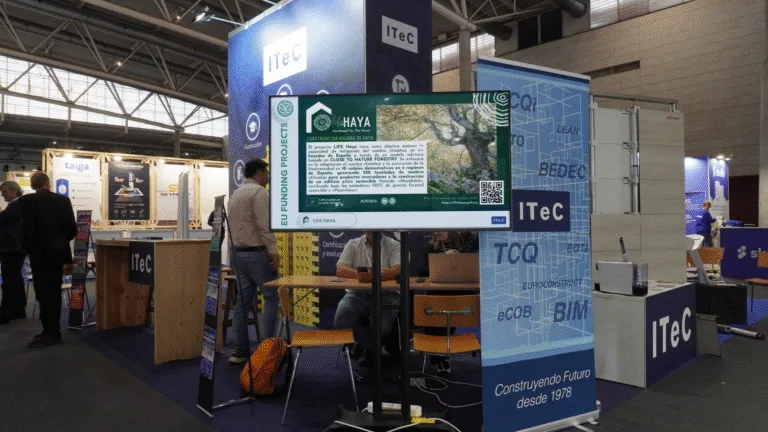 Pantalla informativa del proyecto LIFE HAYA en el stand de ITeC durante la feria Construmat, con panel explicativo y código QR.