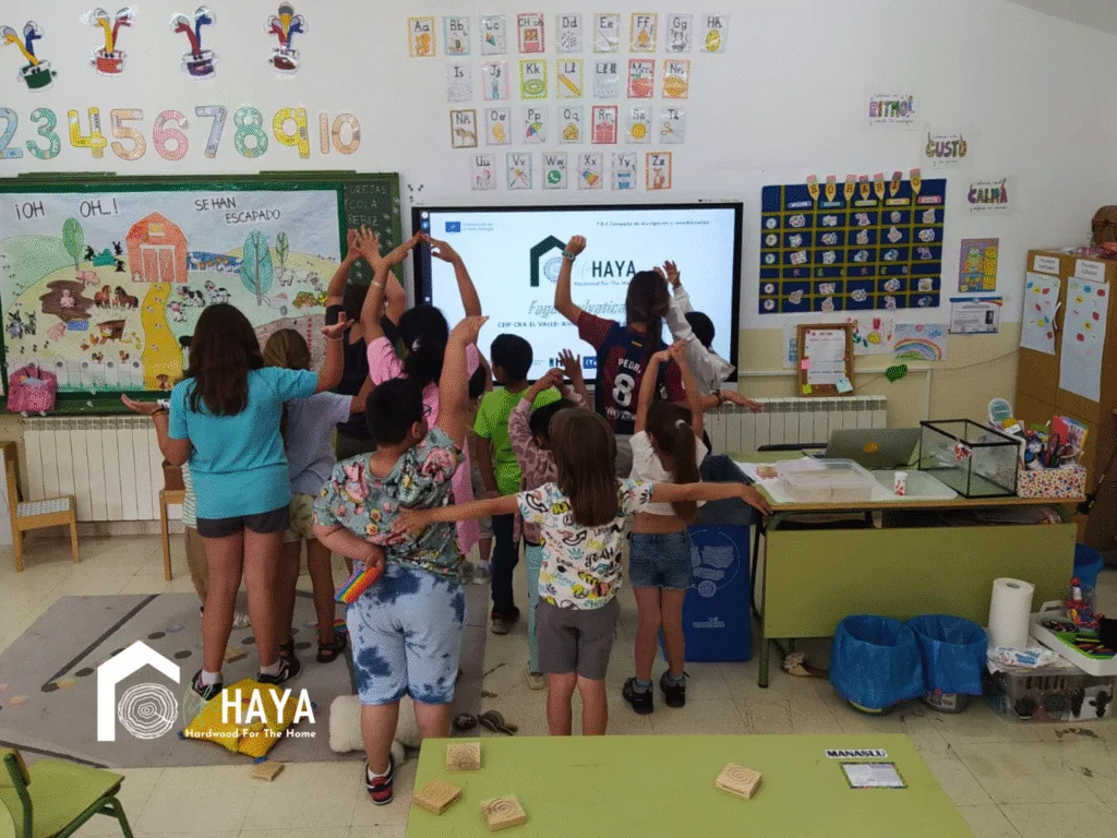 Un grupo de niños de primaria, de pie frente a una pantalla con la diapositiva de LIFE HAYA, celebrando al final del taller.